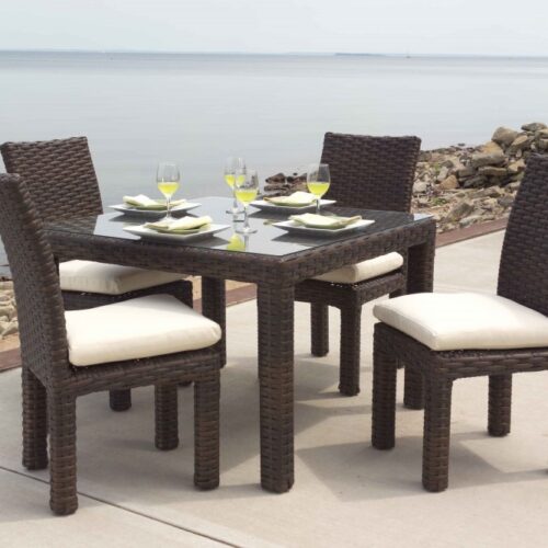 An outdoor dining set with four chairs and a table, neatly set with dishes and wine glasses, located by a tranquil lakeside, featuring an inviting fire pit nearby.