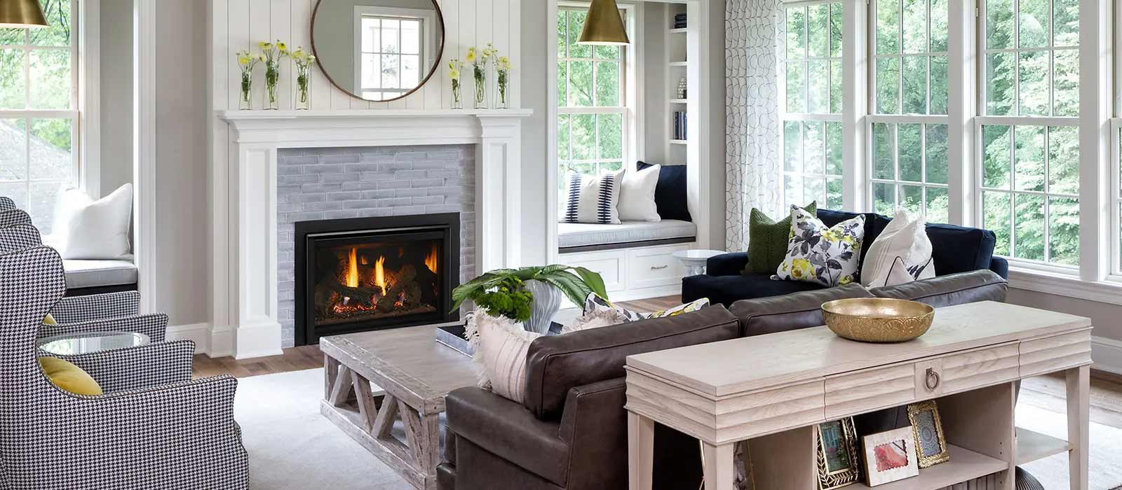 A cozy living room with a lit fire pit, surrounded by comfortable seating and large windows overlooking greenery. The decor includes a neutral color palette with floral accents.