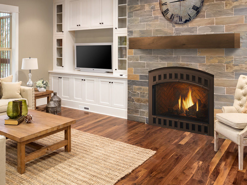 A cozy living room featuring a lit fire pit, stone wall, large wall-mounted tv in a white cabinet, wooden furniture, and comfortable seating arranged on a beige rug.