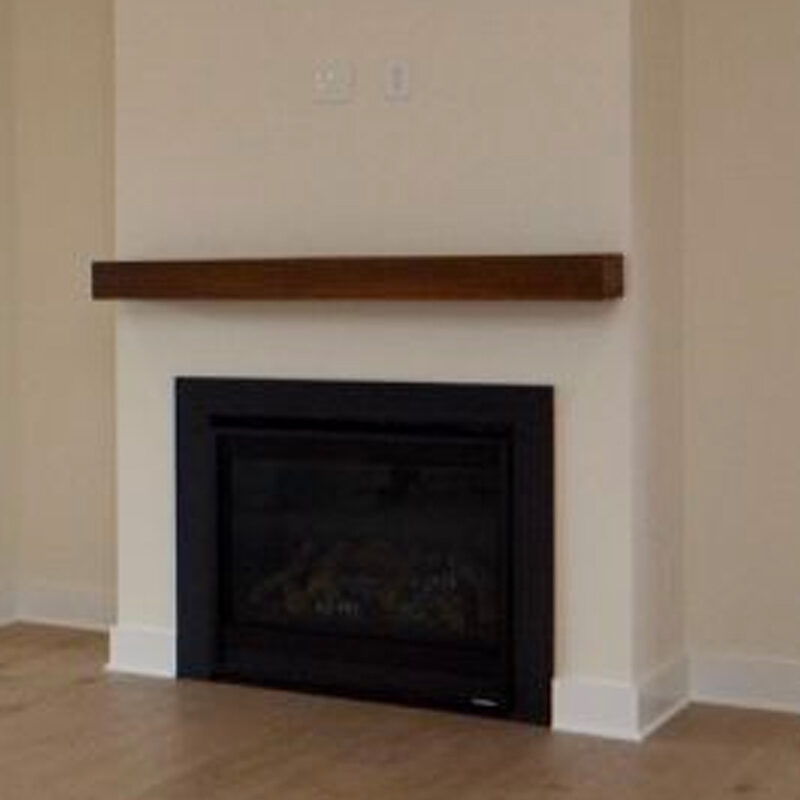 A minimalist room featuring a dark fireplace with a glass front, set below a simple wooden mantel on a plain beige wall. the floor is light-colored.