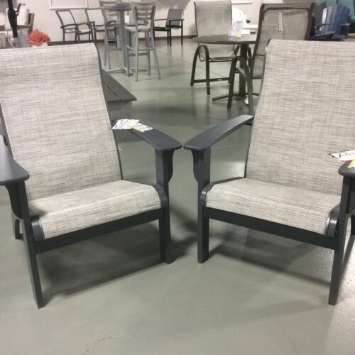 Two gray outdoor chairs with fabric cushions and armrests, facing each other with a small attached table in between, set on a concrete floor in a showroom.
