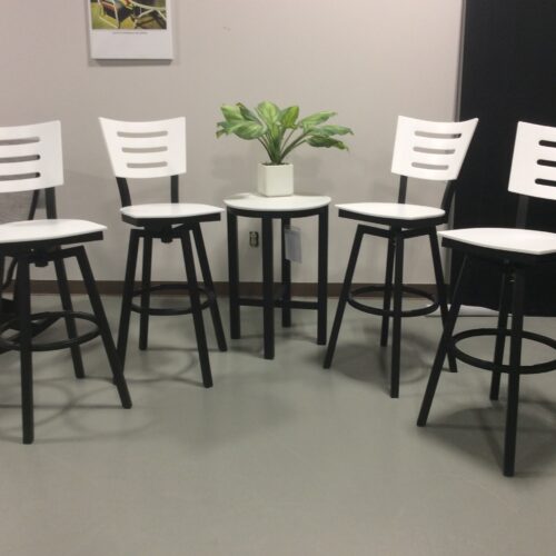 Four white modern bar stools arranged around a small white table with a green potted plant in the center, on a gray floor in a simple interior setting.