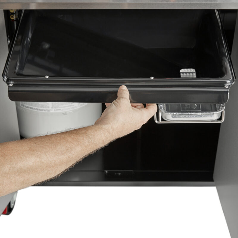 A person's hand opening the front panel of a black Weber Genesis S-435 Four-Burner Natural Gas Grill to access its internal components, showing a view of the burners and other mechanisms inside