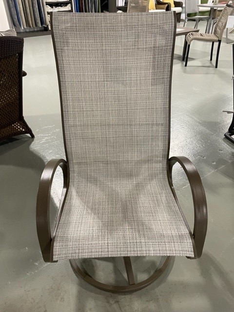 A modern Aruba II rocking chair with a sleek, metallic frame and textured gray fabric, displayed in a showroom with a concrete floor.