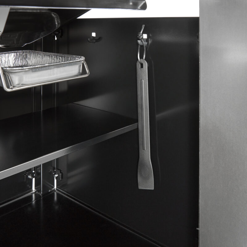A close-up image of a sleek, modern kitchen with a metal spatula hanging from a hook under a black, shiny Weber Genesis S-435 cabinet, reflecting attention to minimalist design.