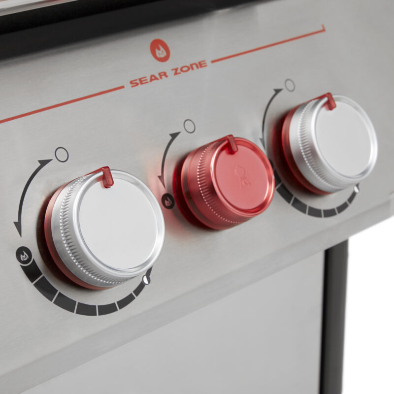Two control knobs on a Weber Genesis S-435 four-burner natural gas grill, with one knob red and the other white, both set to the off position, labeled "sear zone