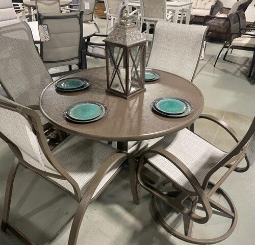 An Aruba II round patio dining set with four chairs in a store, featuring a metal frame and fabric seating, with blue plates and a decorative lantern on the tabletop.