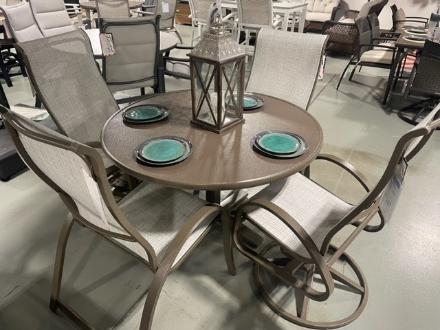 An Aruba II round patio dining set with four chairs in a store, featuring a metal frame and fabric seating, with blue plates and a decorative lantern on the tabletop.