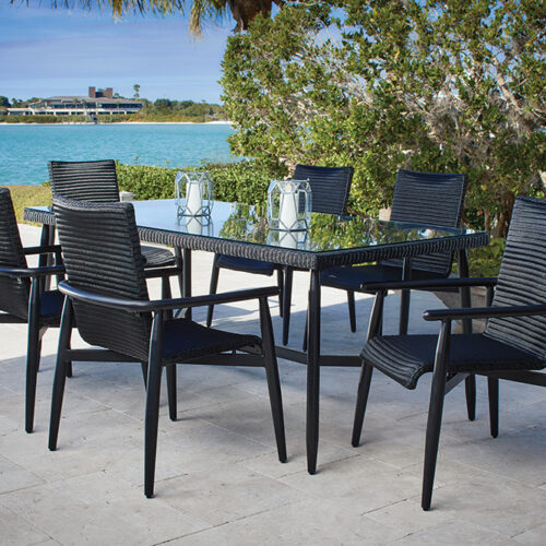 Outdoor dining setup with a modern black table and six chairs on a Fairview patio overlooking a serene lake and greenery. It’s a clear sunny day with a gentle breeze moving the foliage.