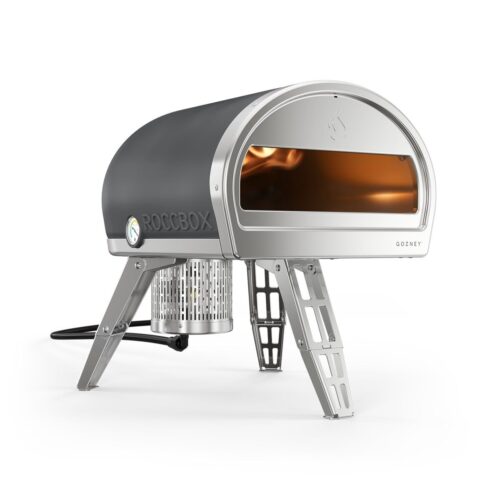A portable Roccbox pizza oven with a stainless steel exterior and foldable legs, featuring a clear view inside through an open front showing a stone baking floor.