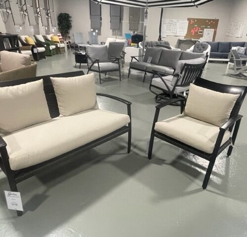 A furniture showroom with various modern chairs and sofas on display, featuring a mix of metal frames and light-colored cushions, set against a grey floor.