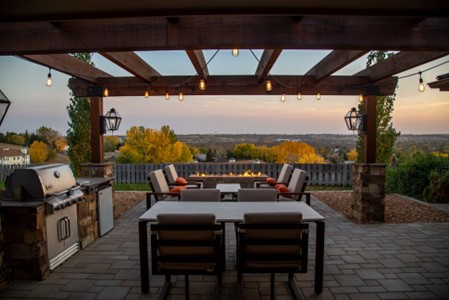 outdoor living space with a gas grill, dining set, lounge furniture, fire table, trees in the background, and sunset-colored sky