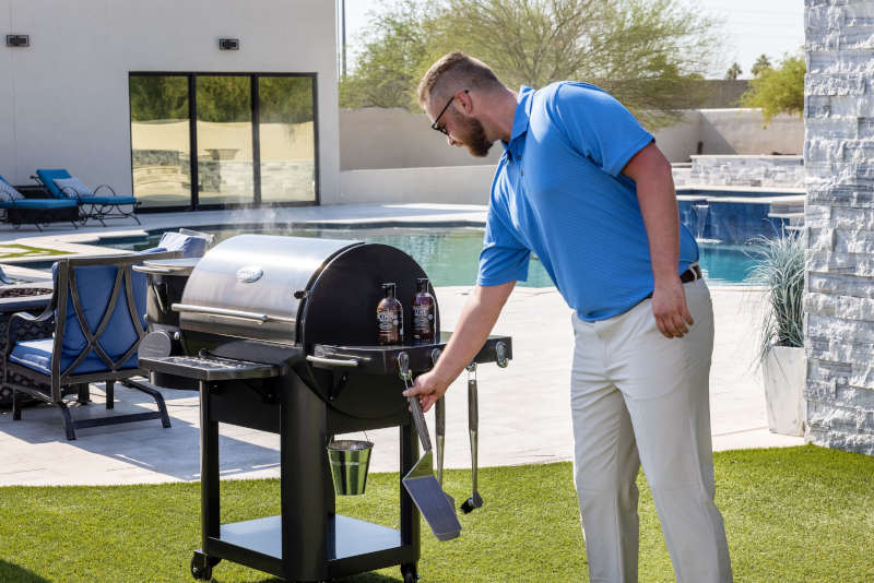 adult man wearing a blue polo and khakis hanging grill tools on the side of a Louisiana Grill®