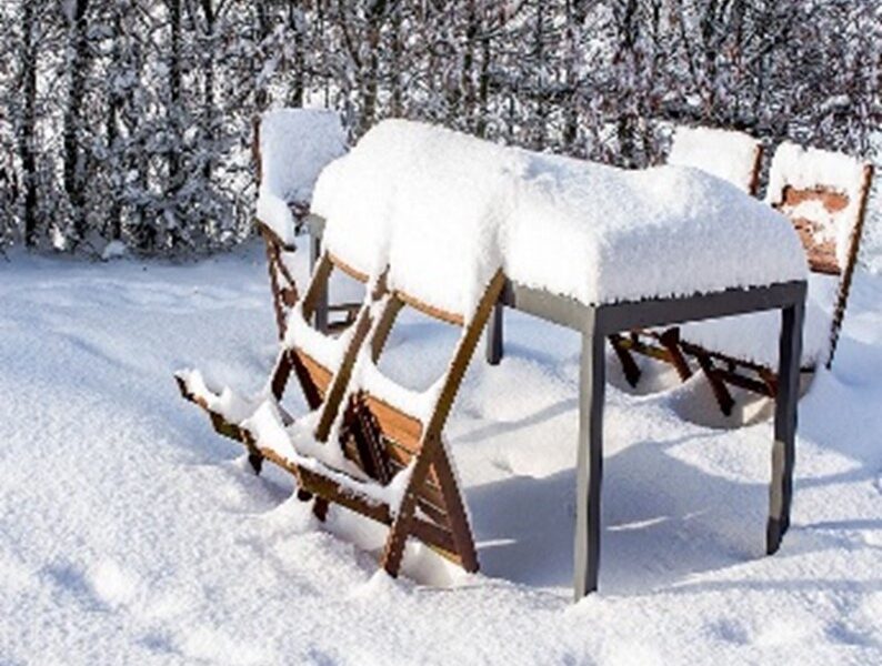 Snow-covered patio, patio table, and chairs; trees in the background