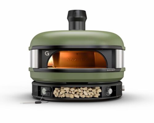 A modern, olive green outdoor pizza oven with a visible fire inside, featuring a front glass door and a chimney on top, set against a plain white background.