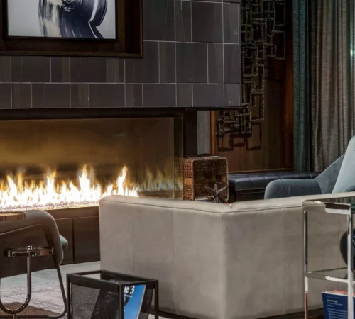 Elegant living room featuring the Enlight Bay Three-Sided Gas Fireplace by Stellar by Heat & Glo, surrounded by stylish furniture including a gray sofa, armchairs, and decorative items.