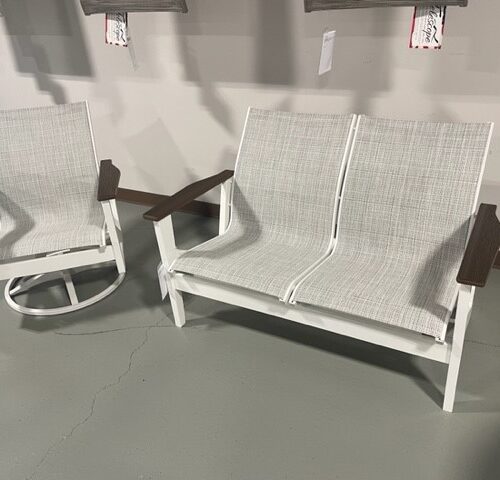 Two modern white outdoor rocking chairs with light gray cushions and Wexler 4 Person Seating Group by Telescope Casual wooden armrests, displayed on a gray concrete floor against a gray wall with paintings