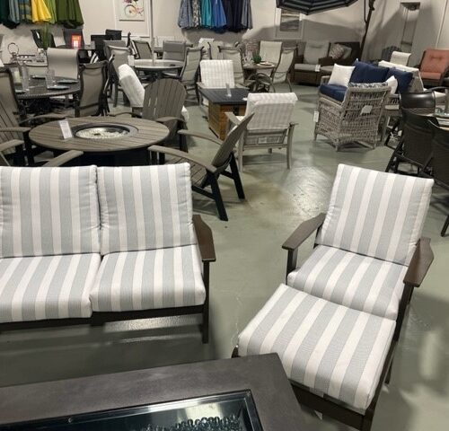 A furniture store displaying various patio sets, featuring two striped cushioned chairs in the foreground, with other chairs and tables arranged in the background.