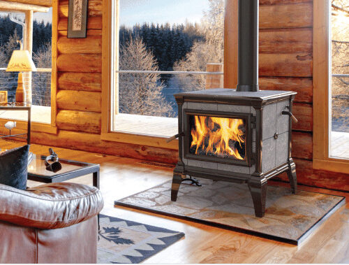 A cozy cabin interior with a lit fireplace, wooded walls, and windows showing a snowy landscape outside. plush seating and warm lighting add to the inviting atmosphere.