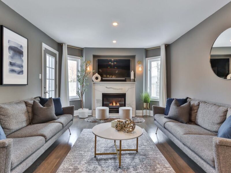 gray couches on either side of a white fireplace, gray painted walls with a round mirror and artwork, an accent rug and round coffee table in the center of the room